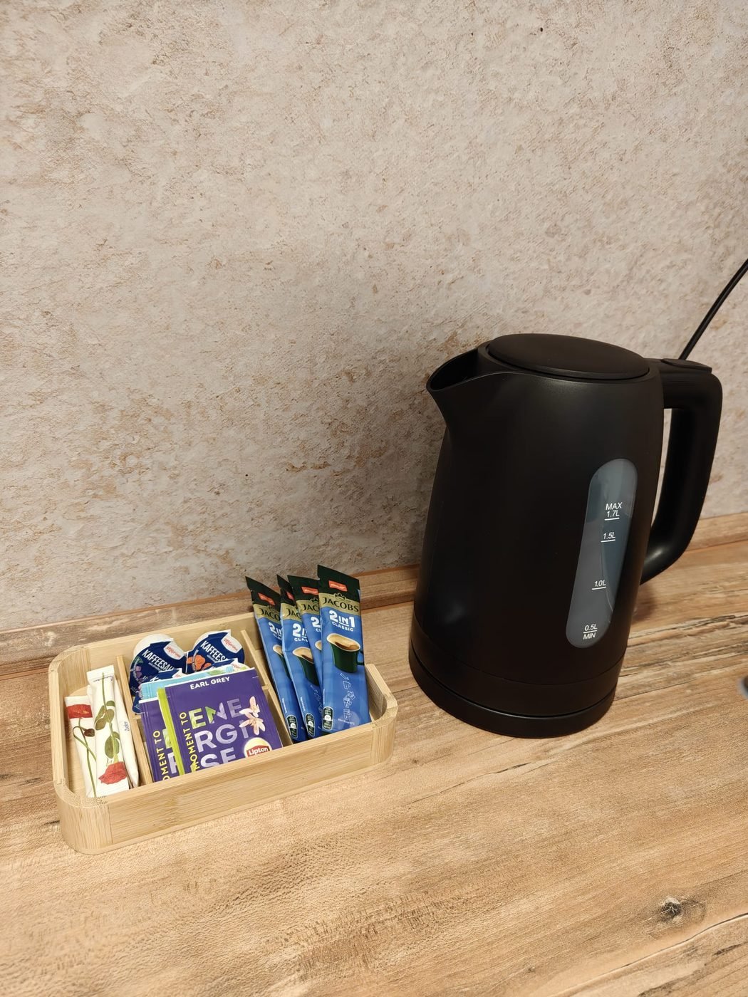 Wasserkocher neben einem Holztablett mit Kaffee, Tee und Zucker
